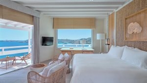 hotelzimmer weiss mit grossen bett und grossen fenstern dazu holz möbeln und einem fernseher vom bett aus hat man durch die offene terrassentür direkten meeresblick auf das azur blaue ozean wasser im luxuriösen hochklassigen exklusiven designer hotel sant